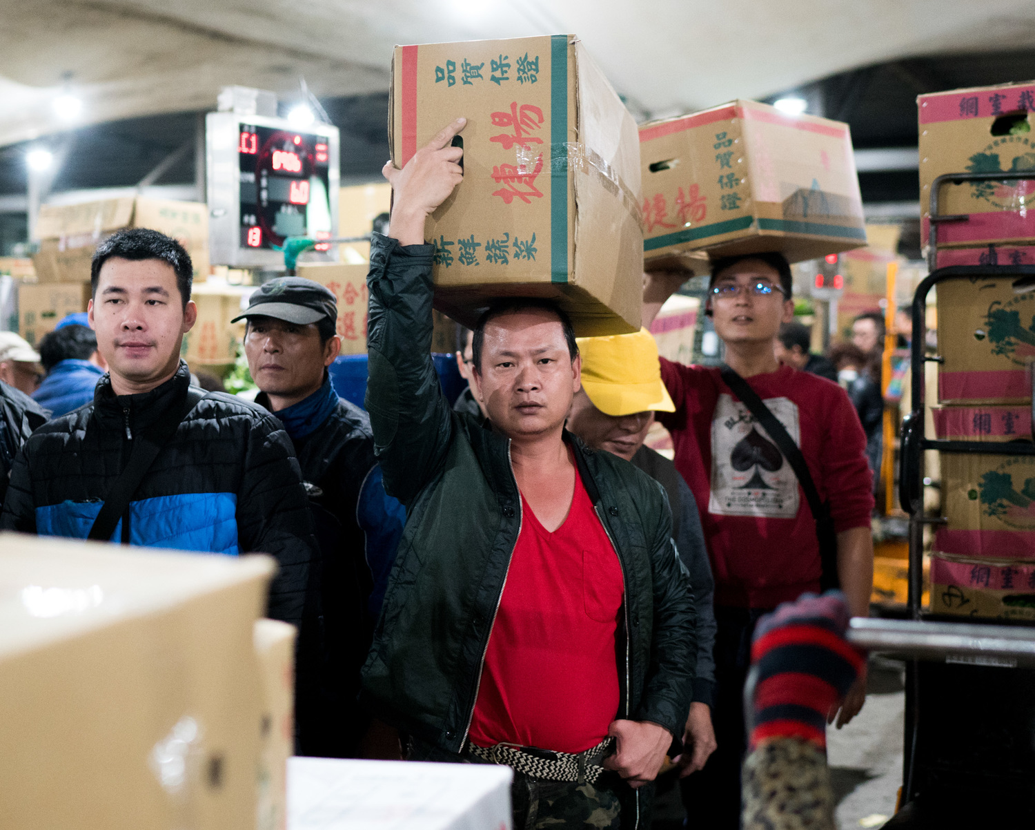 蔬果搬運工人頭頂著紙箱裝的蔬果走在擁擠的通道上。 圖:張良一/攝 蔬果搬運工人頭頂著紙箱裝的蔬果走在擁擠的通道上。 圖:張良一/攝