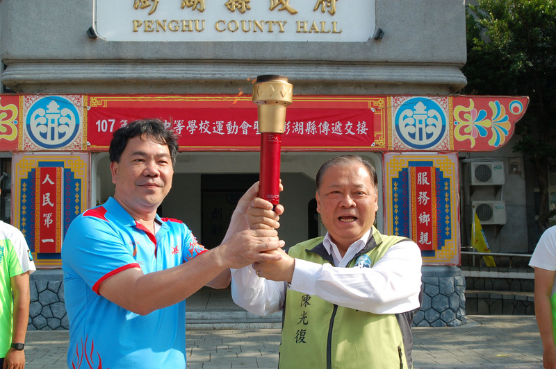 107年全國中等學校運動會聖火16日傳抵澎湖,由台中市南屯區文山國小校長邱炳彰(左)將聖火交接給縣長陳光復(右)後,隨即展開澎湖馬公市區的傳遞。 107年全國中等學校運動會聖火16日傳抵澎湖,由台中市南屯區文山國小校長邱炳彰(左)將聖火交接給縣長陳光復(右)後,隨即展開澎湖馬公市區的傳遞。