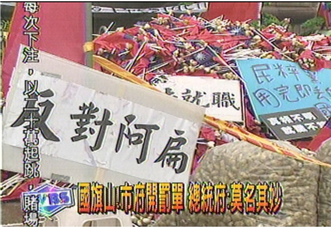 「國旗塚」為2004年之事,「民粹黨用完即丟的國旗」海報清晰可見。 圖:取材自TVBS網站 「國旗塚」為2004年之事,「民粹黨用完即丟的國旗」海報清晰可見。 圖:取材自TVBS網站