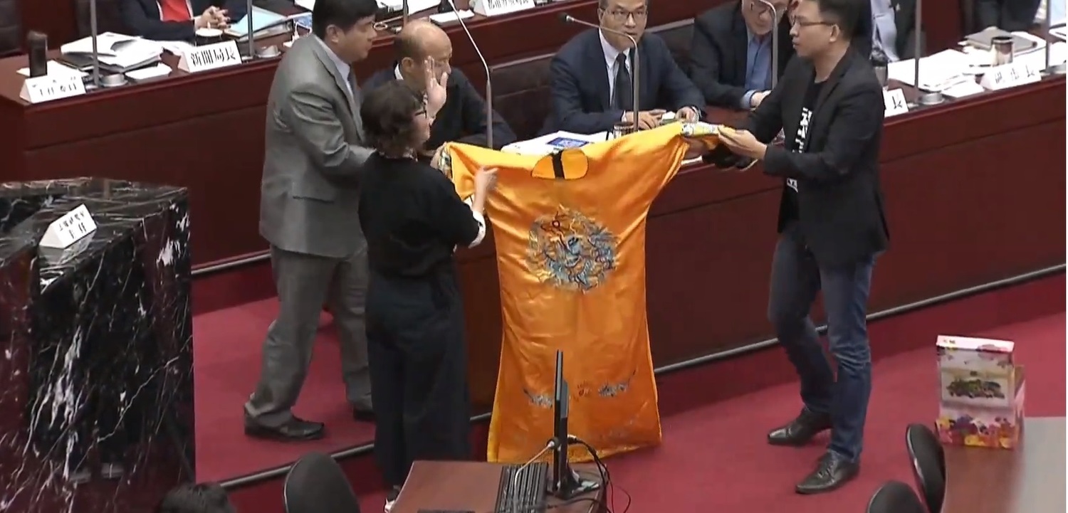 高雄市議會今日開會時,民進黨團總召李喬如及市議員黃文益準備了一件黃袍送給高雄市長韓國瑜。 圖:翻攝自youtube。 高雄市議會今日開會時,民進黨團總召李喬如及市議員黃文益準備了一件黃袍送給高雄市長韓國瑜。 圖:翻攝自youtube。