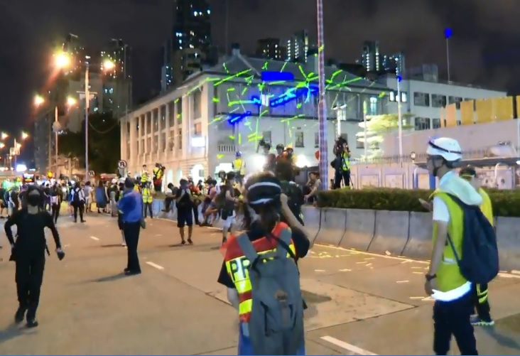 現場有人以雷射筆射向警署外牆,警方要求「雷射攻擊」警署的人馬上停止,否則將進行武力驅散。 圖:翻攝香港電台臉書影片 現場有人以雷射筆射向警署外牆,警方要求「雷射攻擊」警署的人馬上停止,否則將進行武力驅散。 圖:翻攝香港電台臉書影片