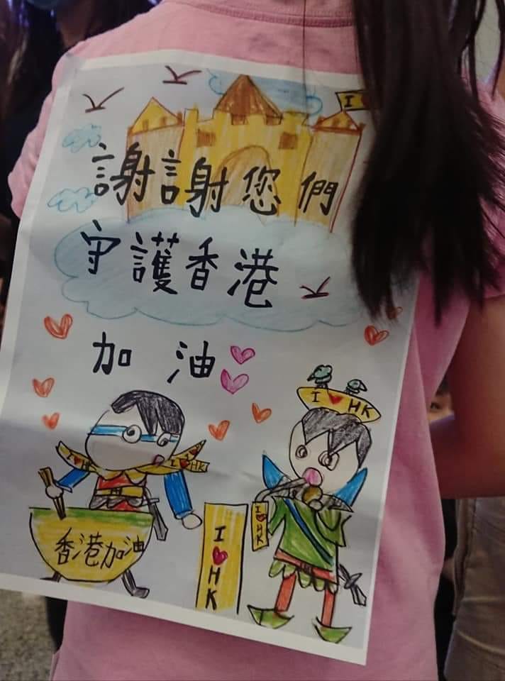 有網友在王丹臉書底下留言,指出當天在機場,還有一名小女孩與兩個小男生,發餅乾給現場留守的市民,背上同樣背著標語,寫著「謝謝您們守護香港」 圖:翻攝自王丹网站 Wang Dan's Page 有網友在王丹臉書底下留言,指出當天在機場,還有一名小女孩與兩個小男生,發餅乾給現場留守的市民,背上同樣背著標語,寫著「謝謝您們守護香港」 圖:翻攝自王丹网站 Wang Dan's Page