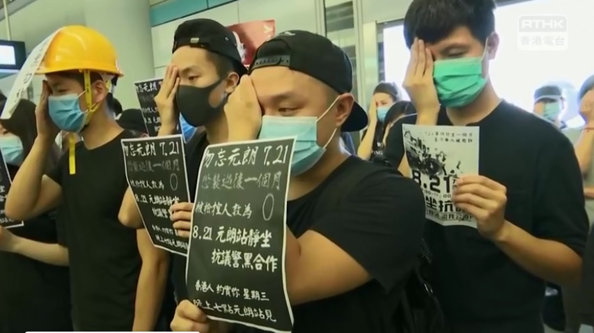 示威者穿黑衣戴口罩,手持「反對警黑合作」標語默站。 圖:翻攝香港電台視像新聞臉書 示威者穿黑衣戴口罩,手持「反對警黑合作」標語默站。 圖:翻攝香港電台視像新聞臉書