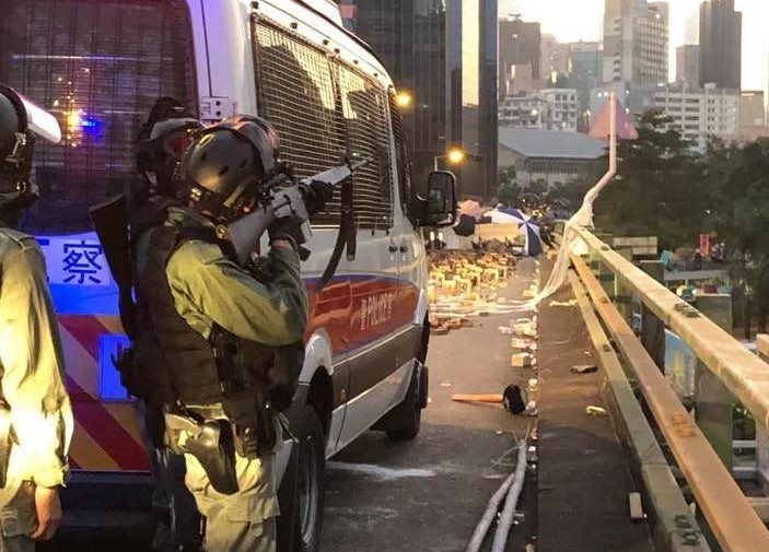港警躲在車後高舉制暴的「最後武器」AR-15實彈步槍指向理工大學。/圖:翻攝自網路 港警躲在車後高舉制暴的「最後武器」AR-15實彈步槍指向理工大學。/圖:翻攝自網路