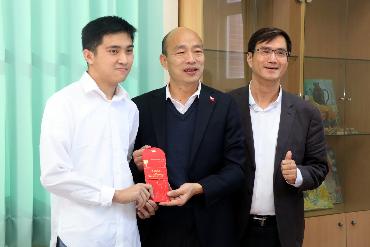 韓國瑜(中)接受原生藝術家王威宏(左)創作的「文創紅包袋」。 圖:高雄市教育局/提供 韓國瑜(中)接受原生藝術家王威宏(左)創作的「文創紅包袋」。 圖:高雄市教育局/提供