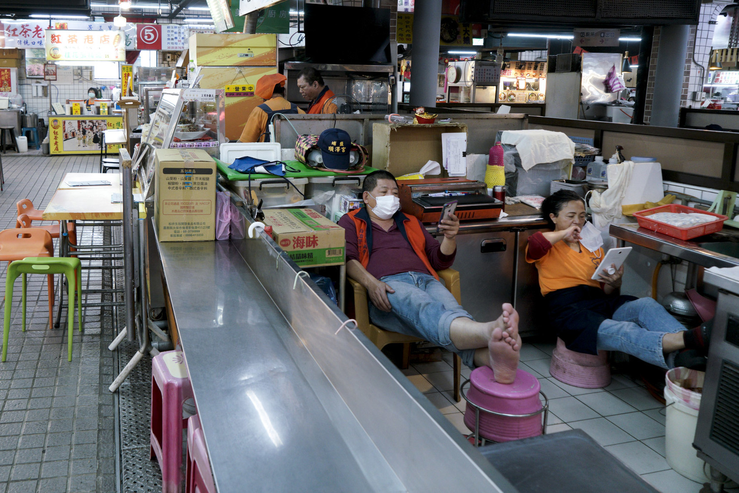 瑞芳美食廣場的攤商利用空檔滑手機。受疫情影響,美食廣場的來客量減少許多。 圖:張良一/攝 瑞芳美食廣場的攤商利用空檔滑手機。受疫情影響,美食廣場的來客量減少許多。 圖:張良一/攝