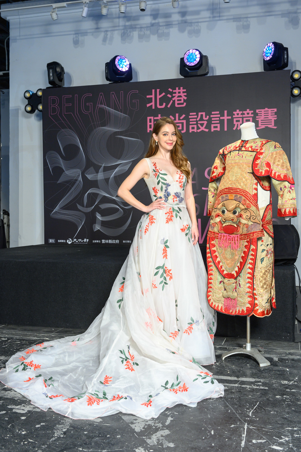 安妮身穿一襲白色刺繡禮服,與集雅軒保存百年戰甲戲服合影。 圖:雲林縣政府文化觀光處/提供 安妮身穿一襲白色刺繡禮服,與集雅軒保存百年戰甲戲服合影。 圖:雲林縣政府文化觀光處/提供