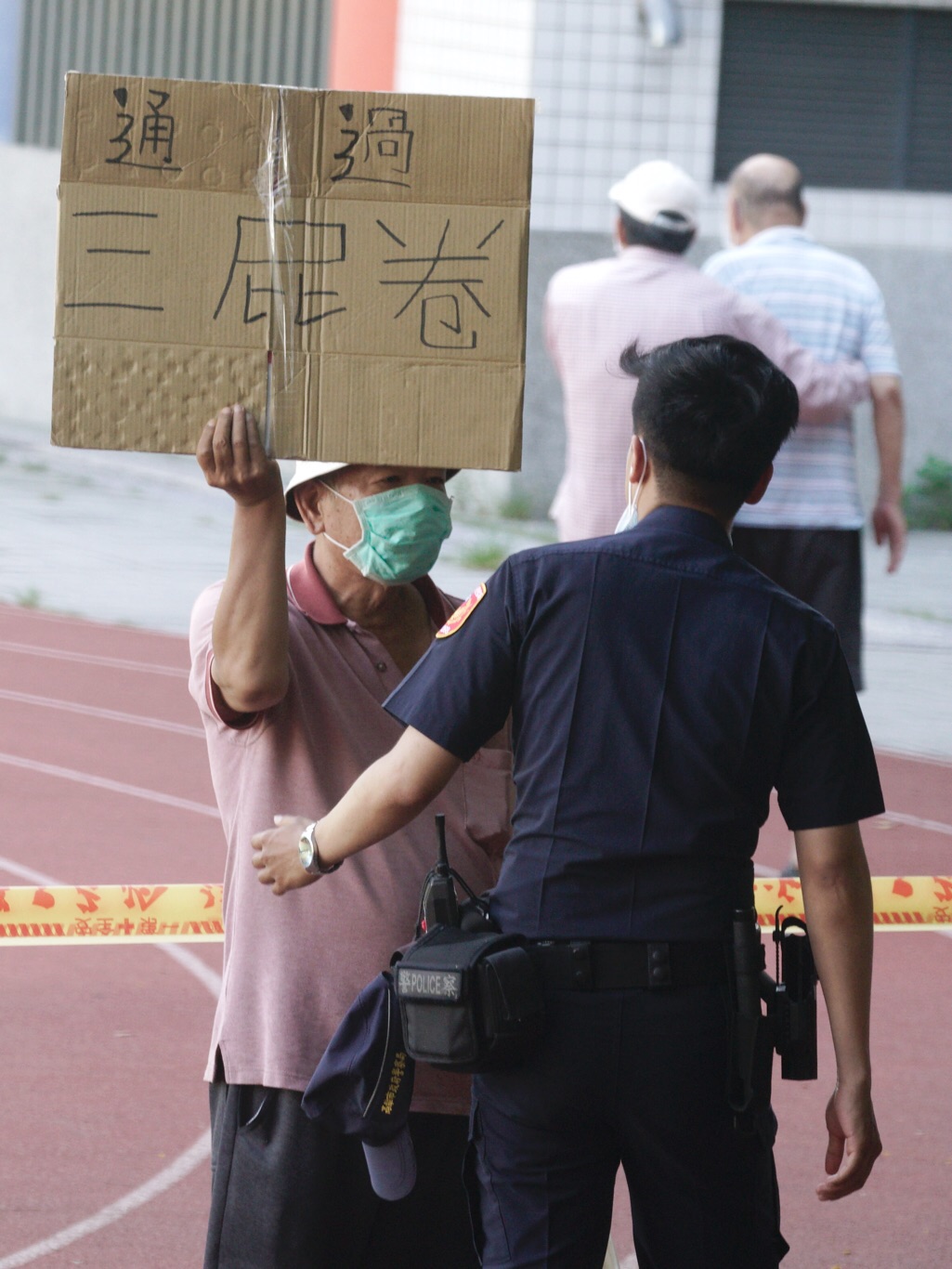 有人在投票所警戒線內高舉「通過三屁卷」,遭警方關切。 圖:張良一/攝 有人在投票所警戒線內高舉「通過三屁卷」,遭警方關切。 圖:張良一/攝