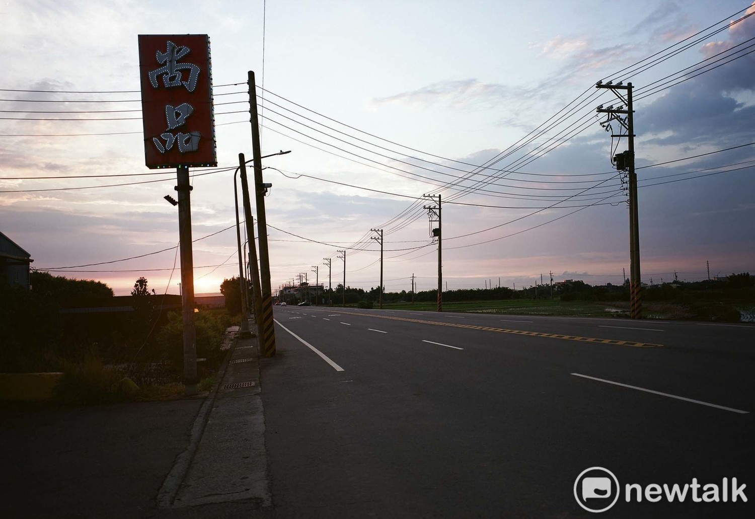 筆直寬闊的四線車道、半空中的廣告看板、電線和電線桿佈滿夕陽餘暉的天際線,空曠的桃園沿海地景中,有著許多不可言說的隱喻。 圖:余白攝影/提供 筆直寬闊的四線車道、半空中的廣告看板、電線和電線桿佈滿夕陽餘暉的天際線,空曠的桃園沿海地景中,有著許多不可言說的隱喻。 圖:余白攝影/提供