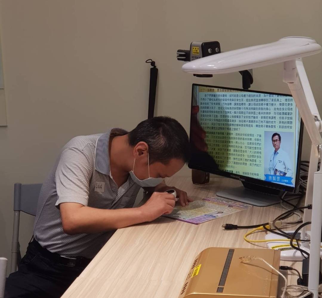 視障者利用放大鏡及桌上型擴視機閱讀文字。 圖:新北市勞工局提供 視障者利用放大鏡及桌上型擴視機閱讀文字。 圖:新北市勞工局提供