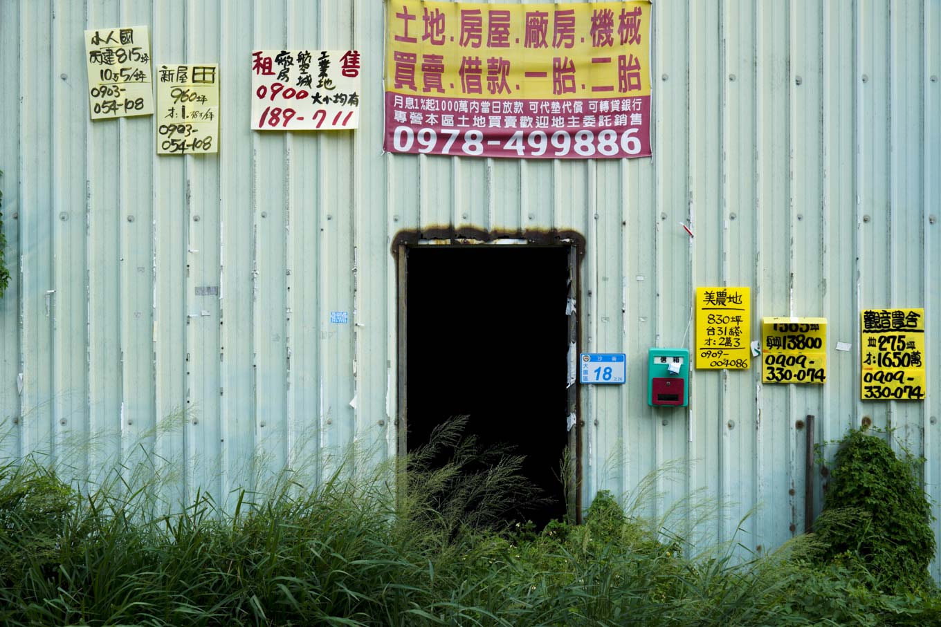 大園區沙崙里的一棟廢棄鐵皮屋,外牆被貼滿了買賣土地的廣告物。 圖:張良一/攝 大園區沙崙里的一棟廢棄鐵皮屋,外牆被貼滿了買賣土地的廣告物。 圖:張良一/攝