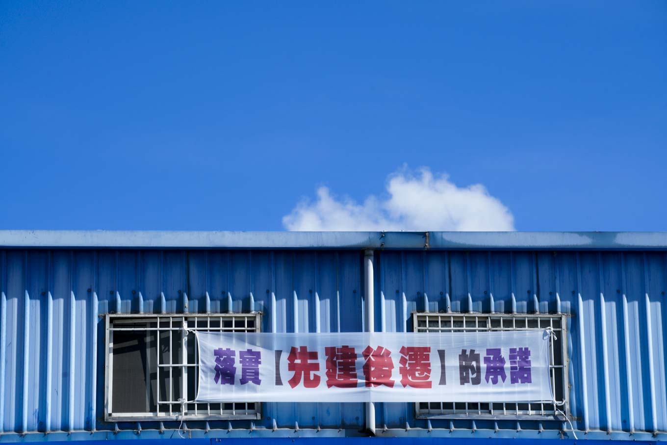 大園區一家汽車修護廠在二樓窗口張貼『落實先建後遷的承諾』的抗議布條。 圖:張良一/攝 大園區一家汽車修護廠在二樓窗口張貼『落實先建後遷的承諾』的抗議布條。 圖:張良一/攝