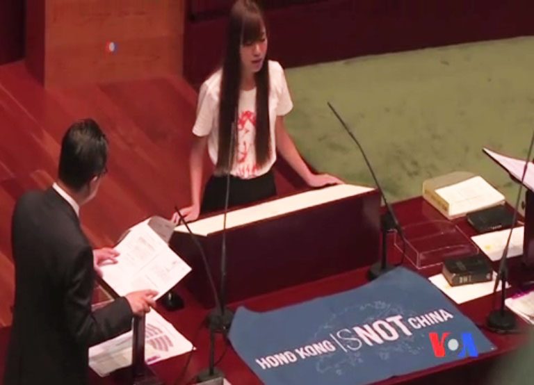 香港新科立法會議員游蕙禎(右)拿出英文寫的「香港不是中國」的藍色布條,進行宣誓。 圖:翻攝美國之音 香港新科立法會議員游蕙禎(右)拿出英文寫的「香港不是中國」的藍色布條,進行宣誓。 圖:翻攝美國之音