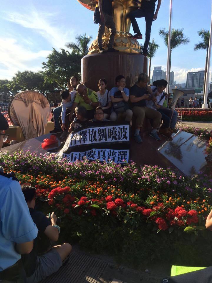 香港眾志約26名成員是在28日下午到金紫荊像,掛上印有「無條件釋放劉曉波,香港市民要真普選」等的黑布標語,一度以鐵鏈纏腰,意圖留守抗議。 圖:翻攝自香港眾志臉書 香港眾志約26名成員是在28日下午到金紫荊像,掛上印有「無條件釋放劉曉波,香港市民要真普選」等的黑布標語,一度以鐵鏈纏腰,意圖留守抗議。 圖:翻攝自香港眾志臉書