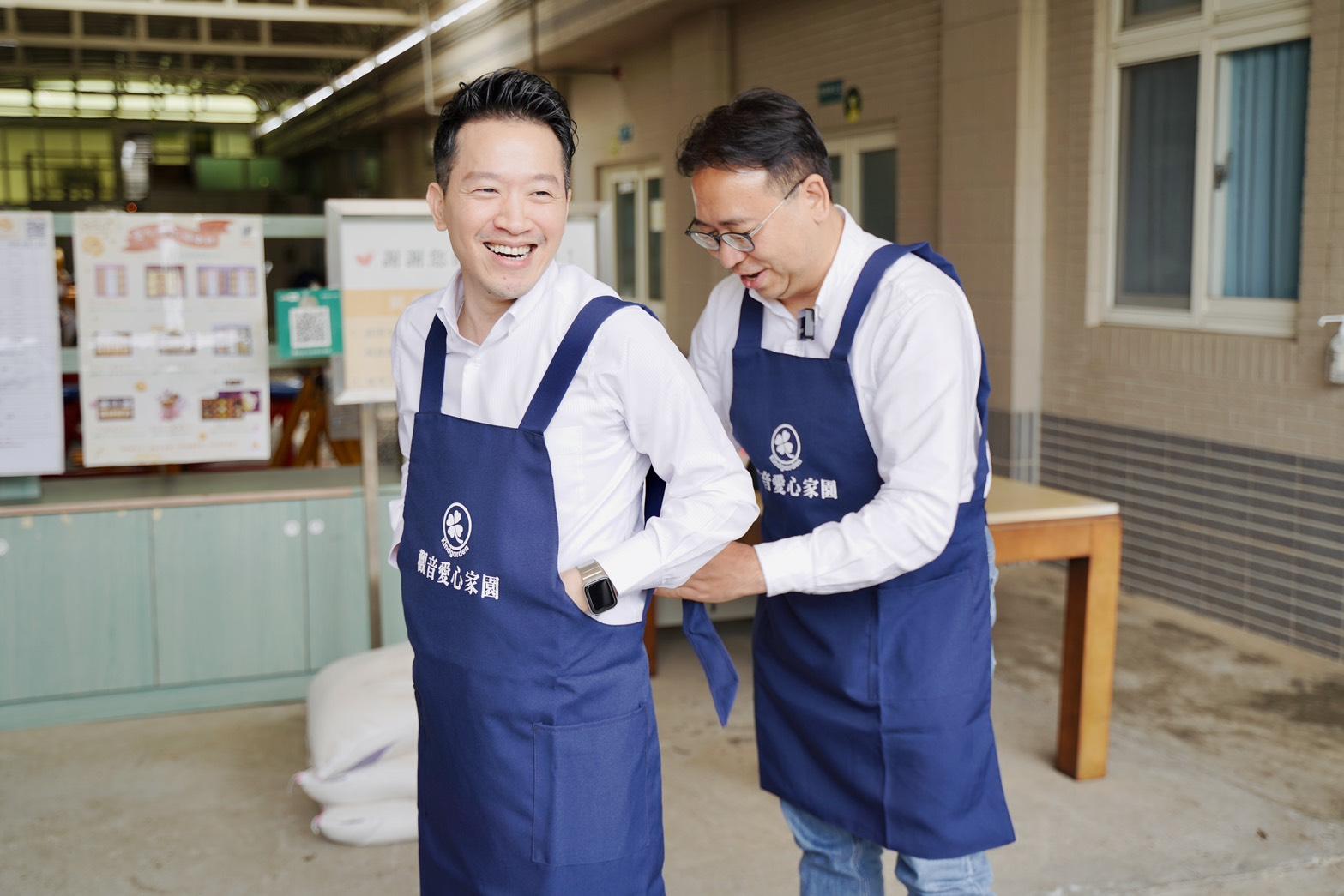 黃世杰與何志偉一同前往觀音愛心家園參訪，並互相替對方綁圍裙。 圖：黃世杰辦公室提供 