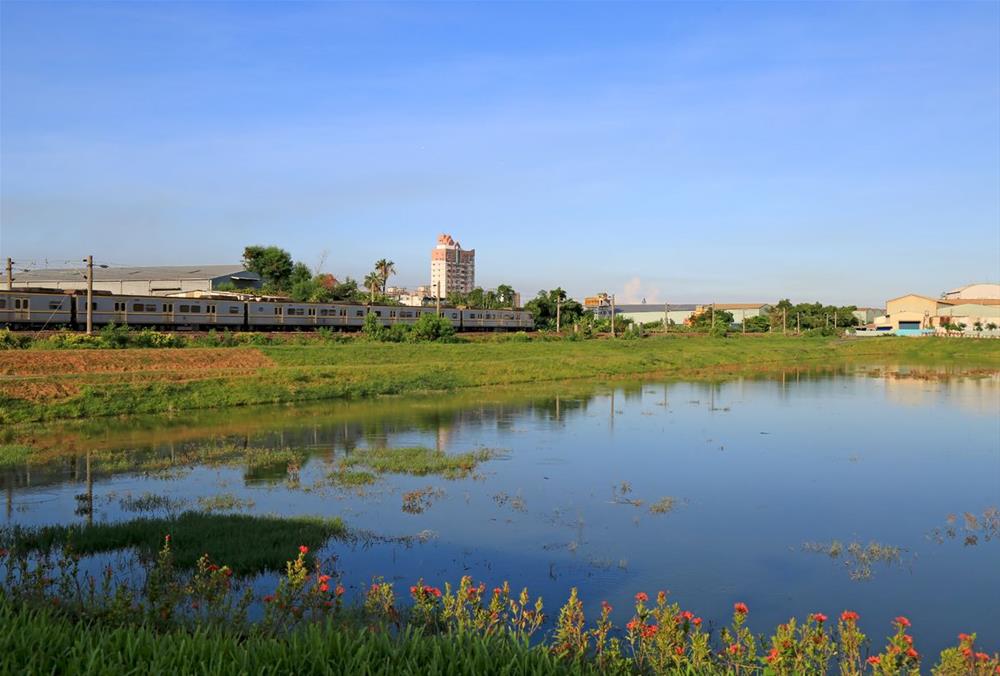 火車駛過鳳山圳滯洪池，水域、鐵路與地方生活交錯。位於大寮、鳥松一帶的滯洪池蓄水量約18萬立方公尺，是原高雄縣區既有治水設施之一。圖：高雄市政府水利局／提供