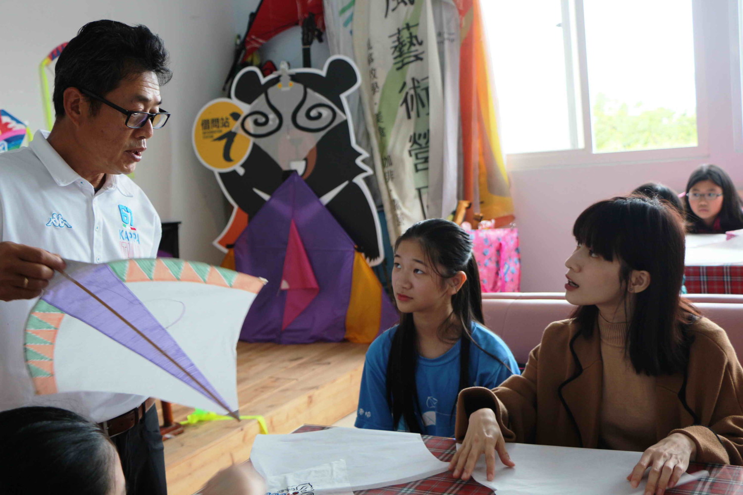 連俞涵和老梅國小學童在風藝術營區風箏高手李青田（左白衣者）協助下，動手合組石門特色的「微風型風箏」和「室內風箏」。   圖：新北市民政局提供