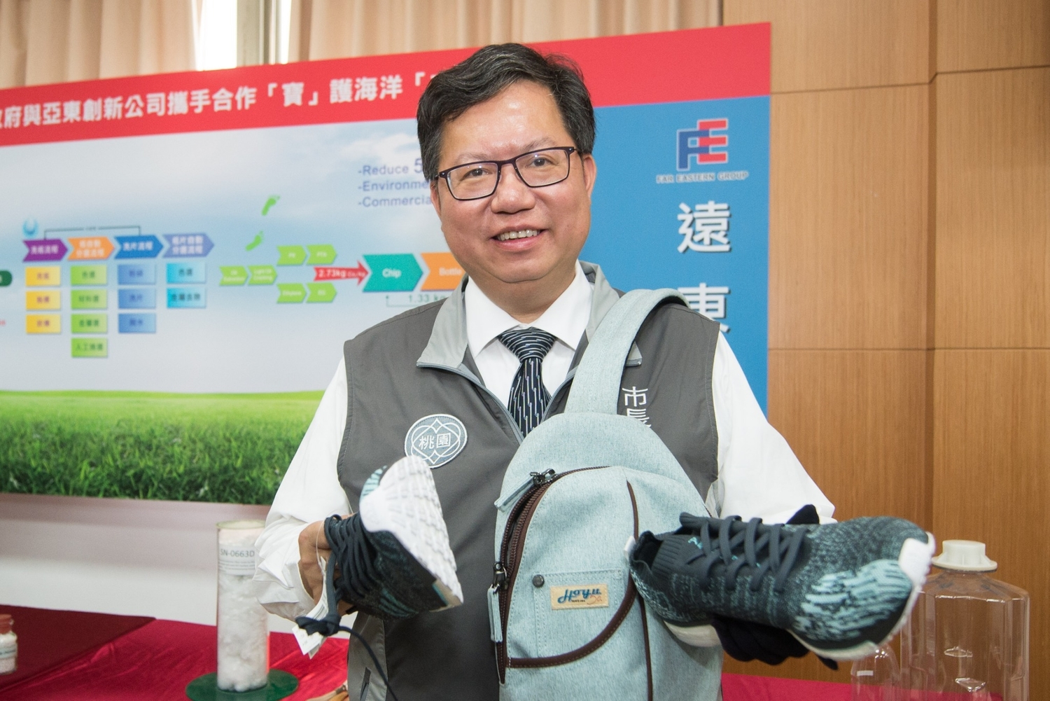 桃園市長鄭文燦手中拿的鞋子和背包都是利用廢棄寶特瓶再生的環保物品。   圖：桃園市政府/提供