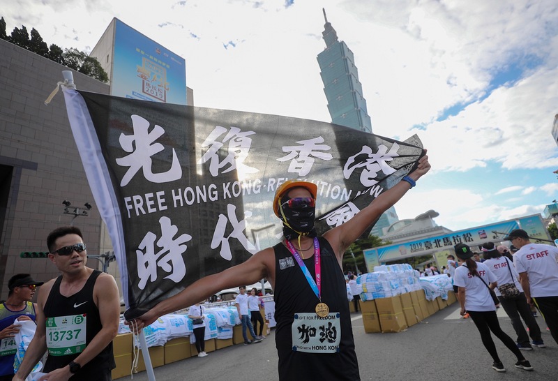 2019台北馬拉松15日在台北市政府前廣場開跑，吸引2萬8000名國內外跑者共襄盛舉，1名跑者完賽後揮舞標語旗幟為香港加油。   圖：中央社提供