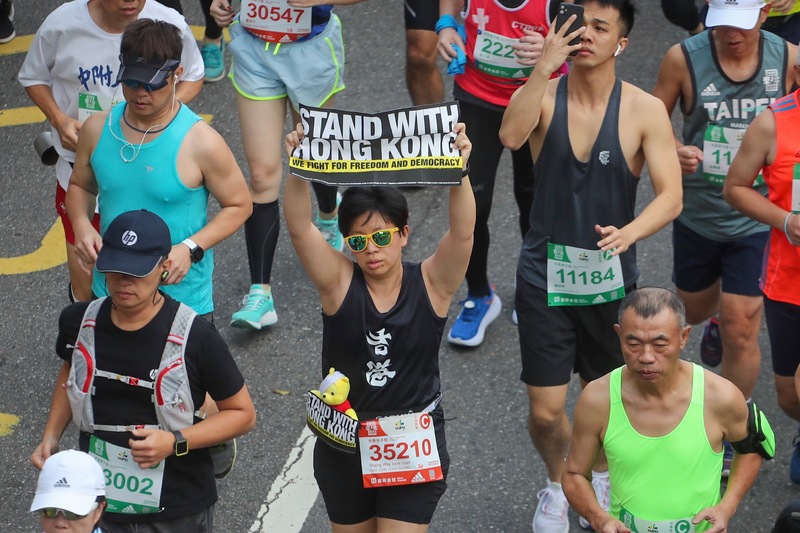 2019台北馬拉松15日在台北市政府前廣場開跑，吸引來自62個國家、2萬8000名國內外跑者報名參與，有跑者手舉支持香港標語參賽。   圖：中央社提供