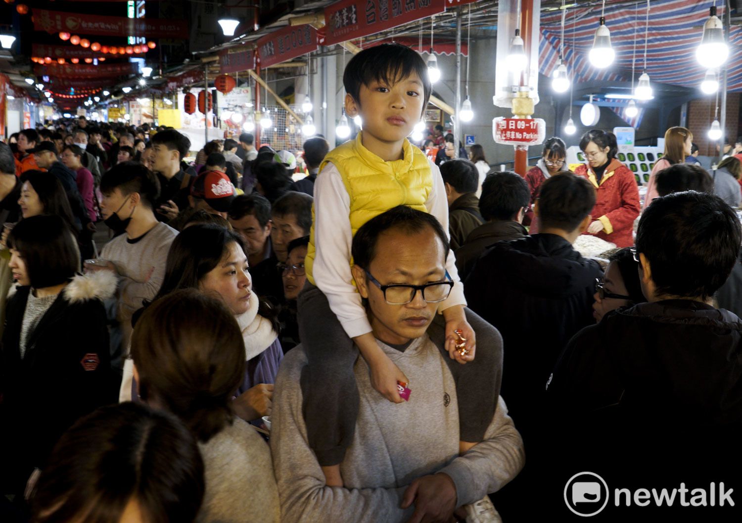 一位小朋友坐著爸爸的肩上，跟著逛年貨大街。   圖：張良一/攝