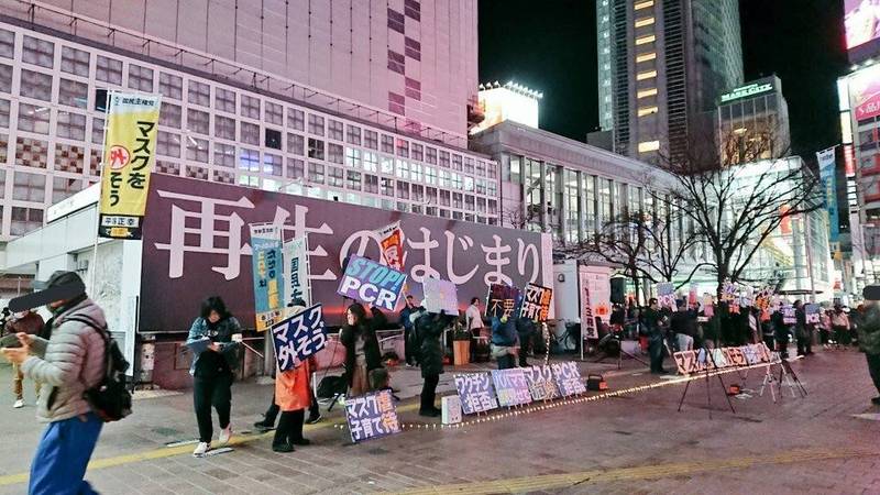 日本武漢肺炎疫情快速升溫，近日網路流傳一張照片，一群人在東京街頭舉標語，呼籲路人「別戴口罩，露出笑容」，並稱新冠肺炎是「為了淨化世界，讓世界重生」。   圖：翻攝自推特