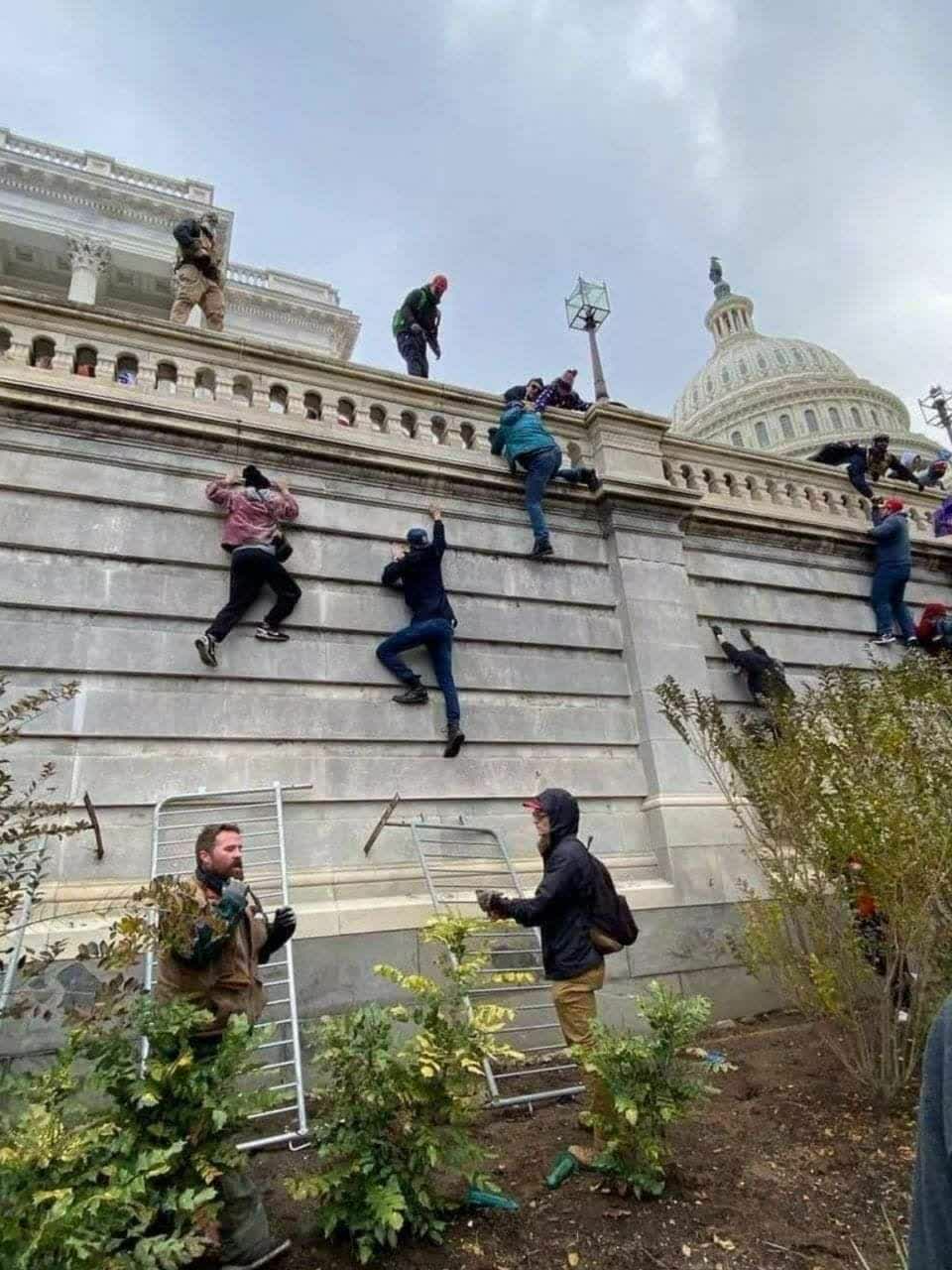 美國暴動民眾爬越國會大樓的高牆，企圖進入議院內。   圖：翻攝自推特