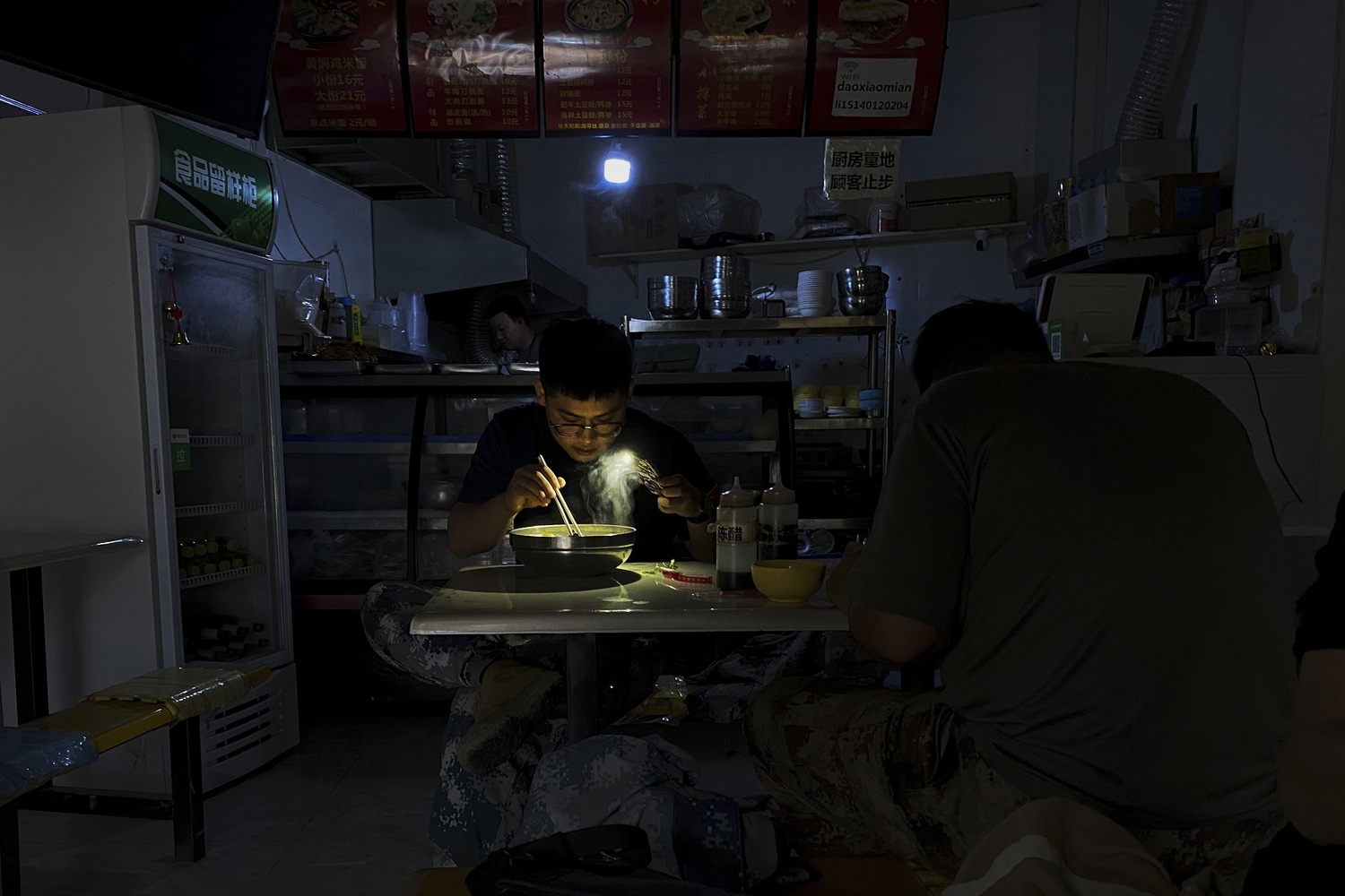 中國東北地區顧客摸黑用餐，只好利用手機的手電筒功能看清碗內食物   圖:達志影像/美聯社