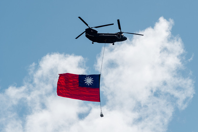 國軍契努克運輸直升機在雙十慶典上，吊掛歷年最大中華民國國旗飛越總統府前廣場上方，成為萬眾矚目焦點。   圖：翻攝自總統府