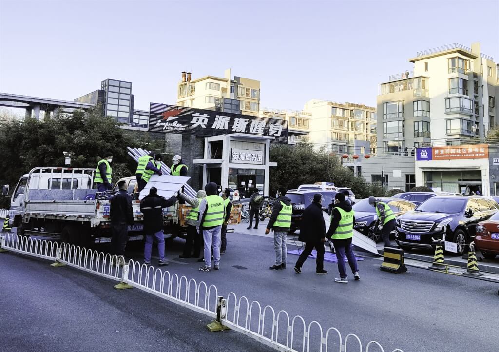 中國北京市15日晚間通報，海淀區新增1例本土確診病例，經基因測序檢出Omicron。圖為工作人員在個案居住的社區門口搭建圍擋。   圖：翻攝中新網