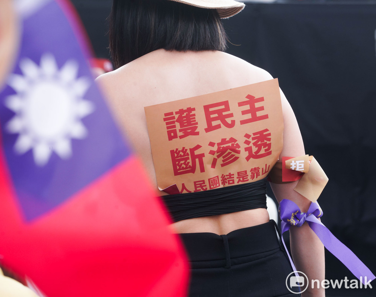 一位女性民眾將『護民主 斷滲透』的牌子在她的衣服背後。   圖：張良一 /攝