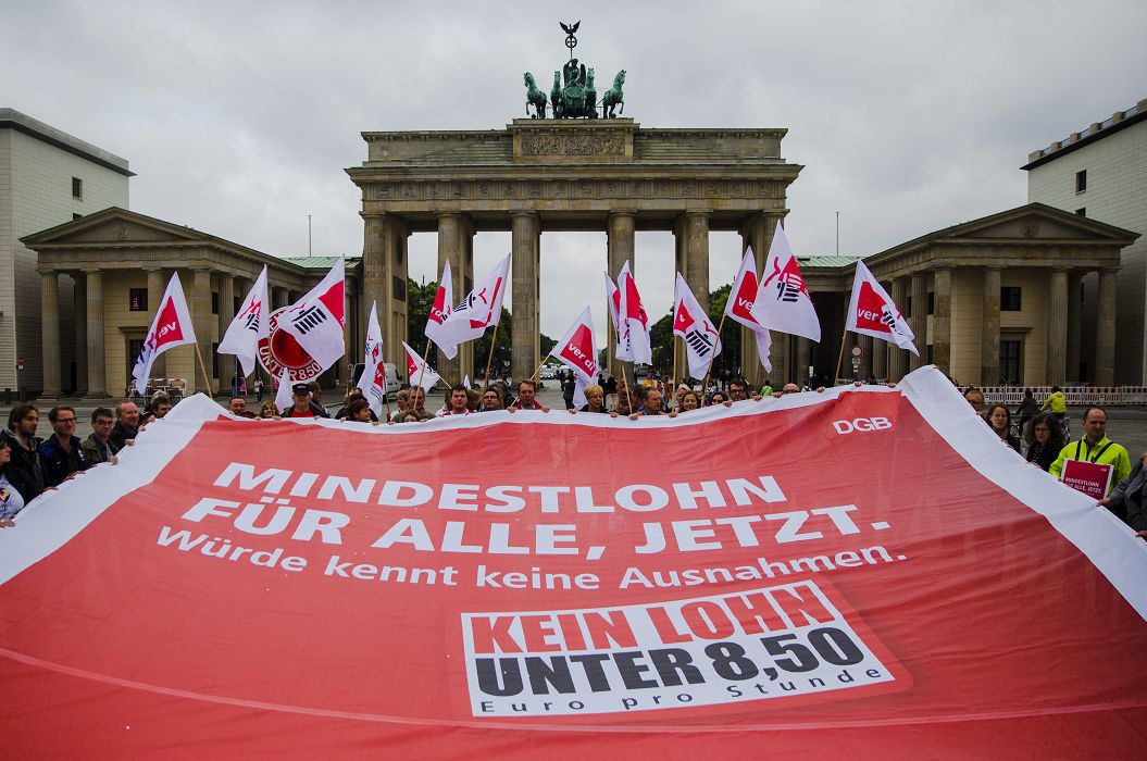 德國民眾在柏林的布蘭登堡門前舉著大幅布條，要求通過全國一體適用的最低工資標準案。圖片來源：達志影像/路透社資料照片   